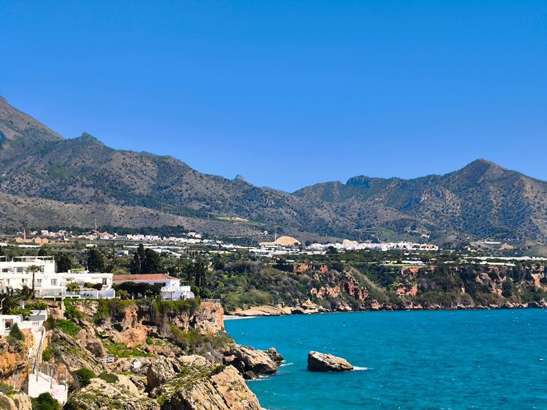 Casas blancas en acantilados junto al mar azul con montañas bajo un cielo despejado.