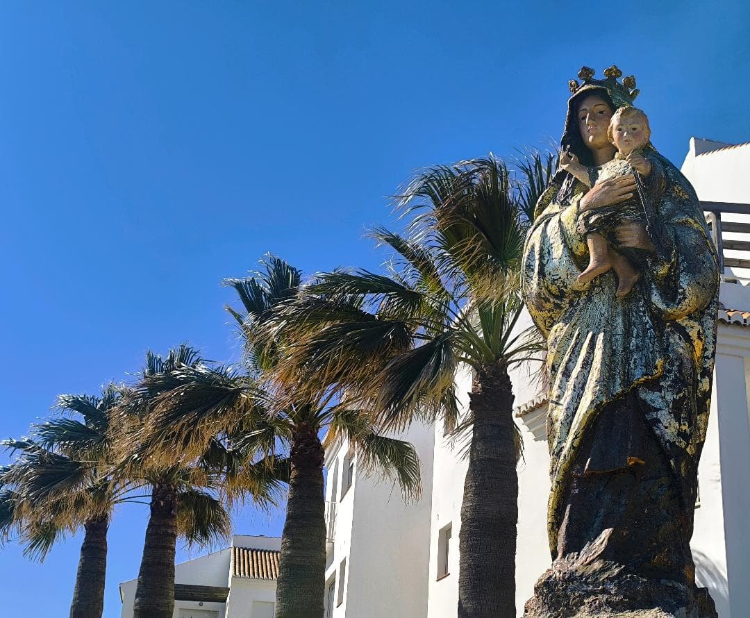 Estatua de la Virgen María y el Niño Jesús ante palmeras y cielo azul.